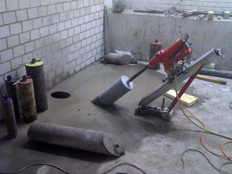 Kernbohrgerät auf einer Bodenplatte, daneben Bohrkronen und ein gezogener Bohrkern