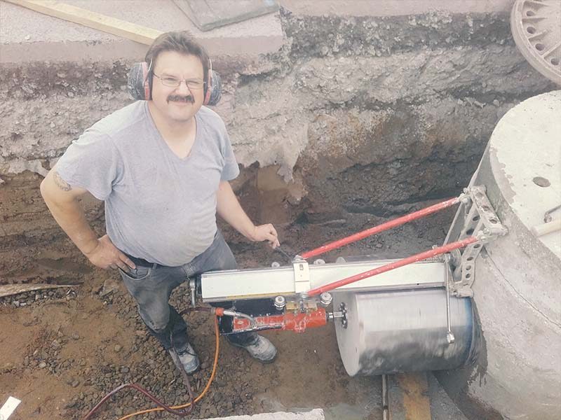 Großes Kernbohrgerät an einem Betonschacht in der Baugrube, daneben der Bohrtechniker mit Gehörschutz